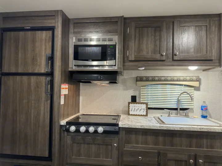 RV rental interior showcasing a compact kitchen with Dometic fridge, High Pointe microwave, stove, sink, and ample dark wood cabinetry.. Starcraft Autumn Ridge Outfitter 2020