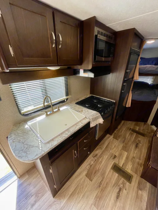 An RV rental's inviting interior, showcasing a modern kitchenette with a sink, stove, microwave, and bunk beds.. Keystone RV Springdale Eco-Lite 2018