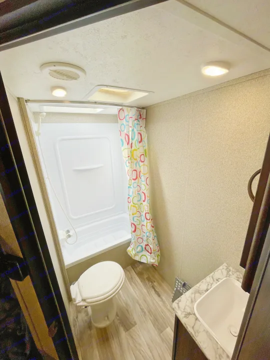 This RV rental bathroom features a compact shower, toilet, and sink with a colorful curtain.. Keystone RV Springdale Eco-Lite 2018