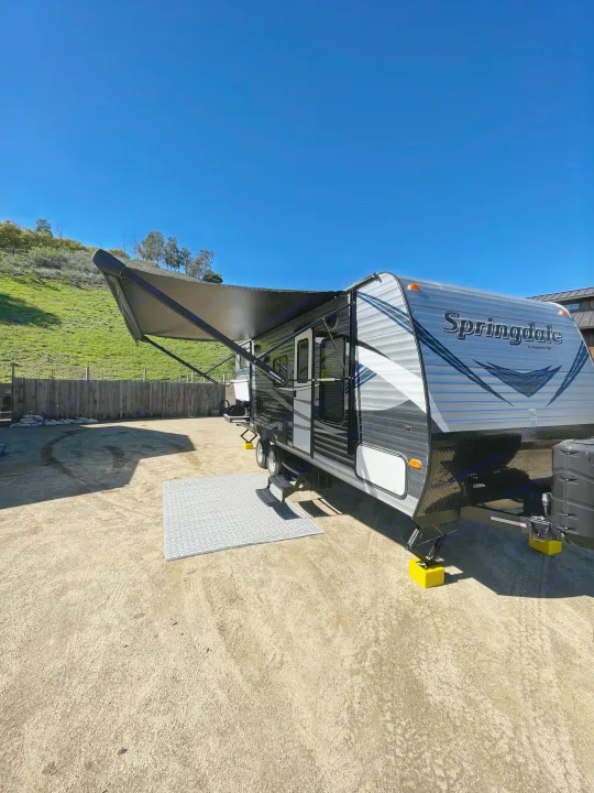 Gray Springdale RV with extended awning on a dirt lot, supported by yellow blocks. Ideal for an RV rental getaway.. Keystone RV Springdale Eco-Lite 2018
