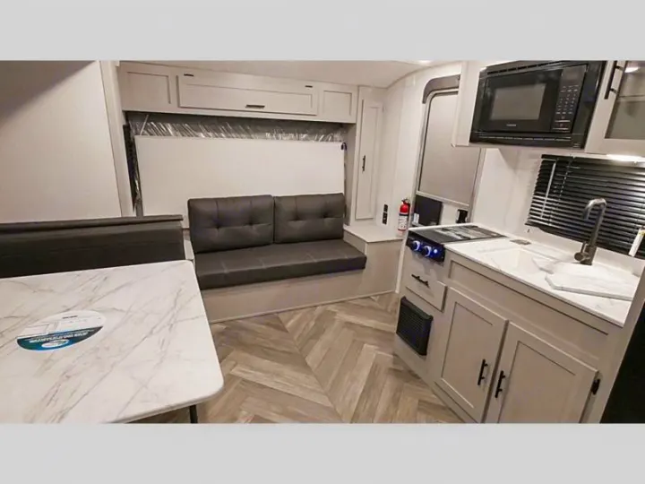 Inside a cozy RV rental: kitchen with microwave, sink & stove, plus a sofa, and dining table.. Forest River Salem FSX Plantium 2022
