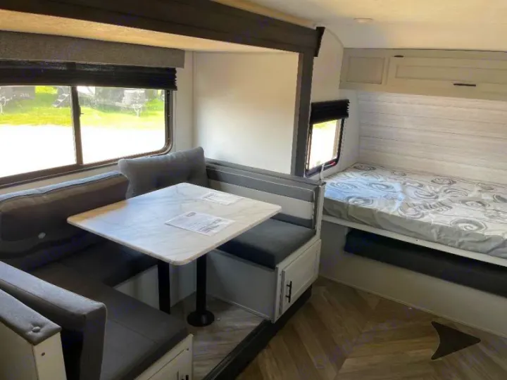 This RV rental interior shows a dinette with a marble-top table and seating, next to a cozy bed.. Forest River Salem FSX Plantium 2022