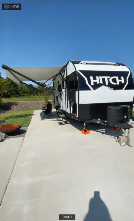 This RV rental is set up for outdoor leisure, featuring an extended awning, chairs, and a fire pit on a sunny day.. Cruiser RV Hitch 2022