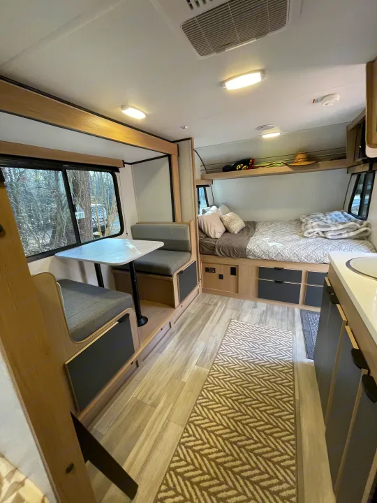 This rv rental interior features a dinette, sleeping area with bed, overhead bunk storage, and a kitchen counter. Bright and functional.. Cruiser RV Hitch 2022