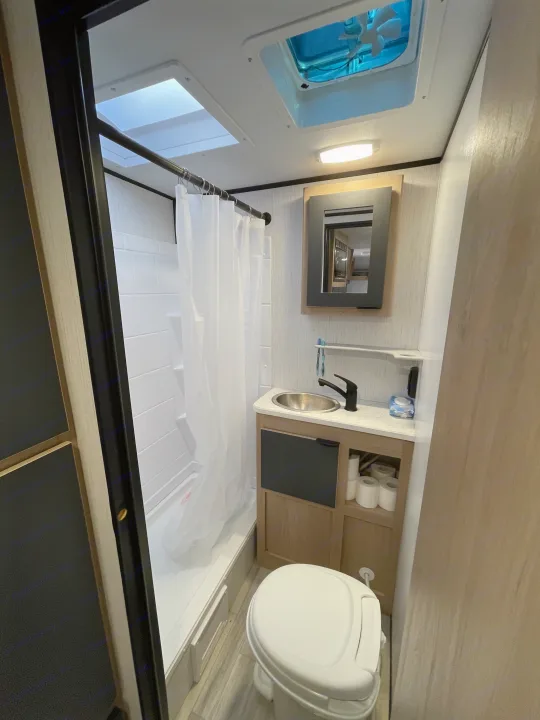 Compact RV rental bathroom features a shower, toilet, sink, and overhead skylight, designed for efficient travel.. Cruiser RV Hitch 2022