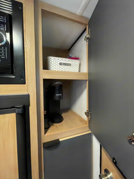 Organized RV rental kitchen: microwave, compact fridge, open cabinet with Keurig coffee maker & storage basket.. Cruiser RV Hitch 2022