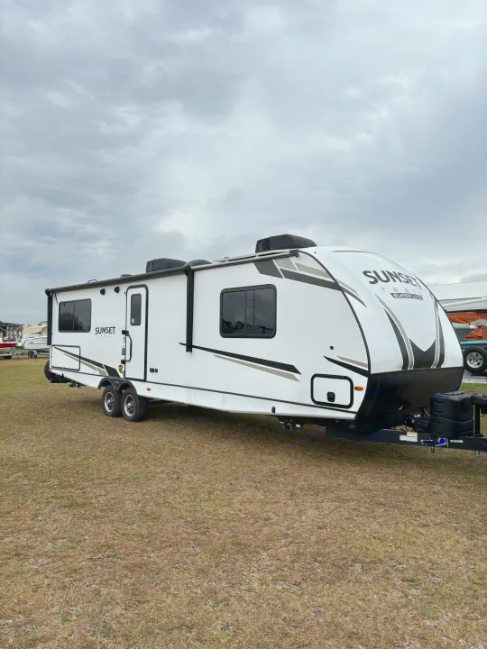 A white "Sunset Trail" RV travel trailer is parked on dry grass under a cloudy sky, ideal for an rv rental.. Crossroads RV Sunset Trail Super Lite 2023