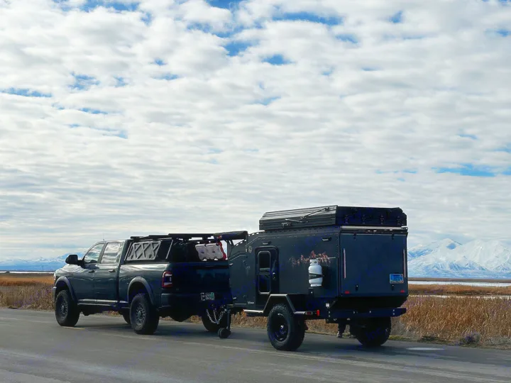 Dark truck towing an overland camper trailer on a scenic road with mountains. Perfect for your RV rental adventure.. Other Other 2024