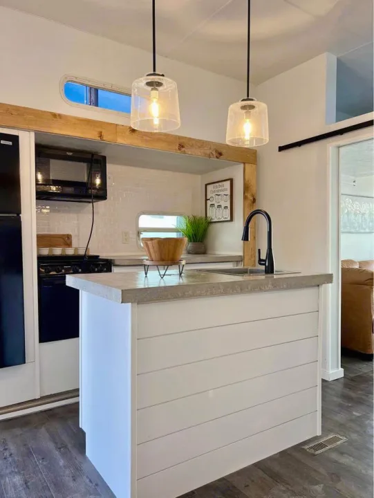 Modern RV rental kitchen. Bright space with shiplap island, concrete-look counter, black appliances, and pendant lights.. Forest River Sierra Sport 2007