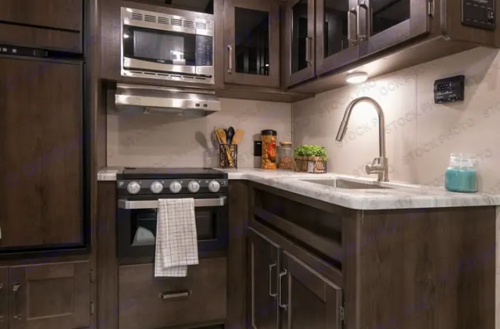 Modern RV rental kitchen showcasing a microwave, stove, and sink. Dark wood cabinetry and stainless steel appliances.. Grand Design Transcend Xplor 2022