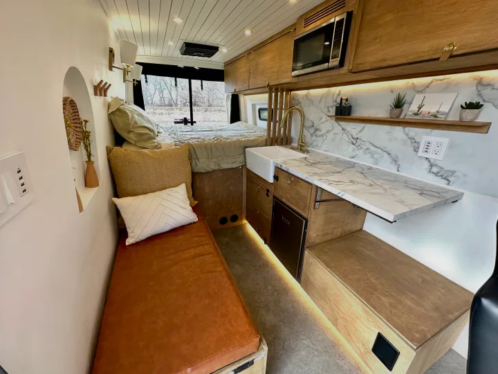 Modern RV rental interior with compact kitchen, cozy bed & bench seating. Stylish mobile living.. Mercedes-Benz Sprinter High Roof Medium wheelbase 2021