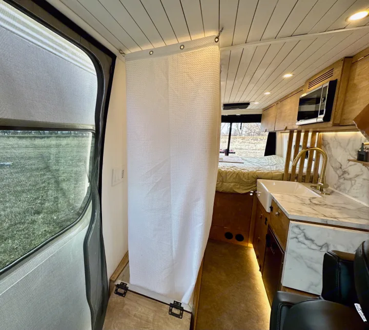 Modern RV rental interior with a kitchen (marble counter, sink, gold faucet), a drawn shower curtain, and a rear bed.. Mercedes-Benz Sprinter High Roof Medium wheelbase 2021