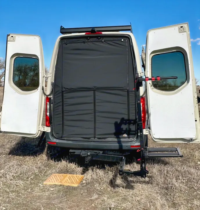 Rear view of an RV rental camper van with open doors, showing a privacy screen and a hitch-mounted bike rack.. Mercedes-Benz Sprinter High Roof Medium wheelbase 2021