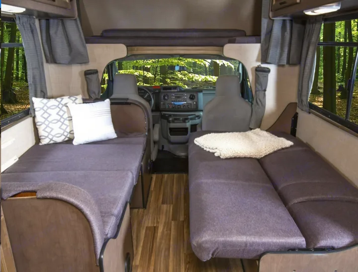 RV rental interior: A compact living space with two beds facing each other, surrounded by windows offering forest views.. Thor Majestic 2018
