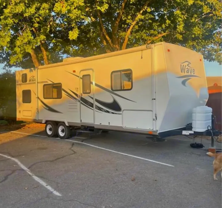 White "Wave" travel trailer RV rental parked in a lot under trees, illuminated by sunlight. Ready for your next adventure.. Thor Motor Coach Wave 2007