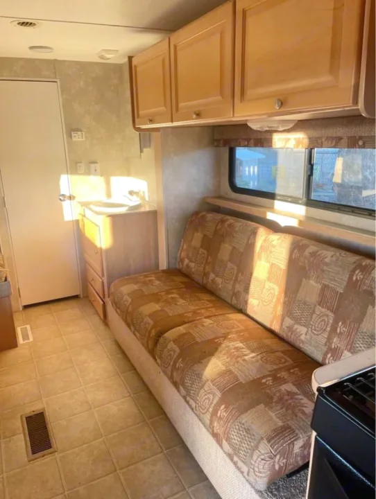 Cozy RV rental interior featuring a patterned sofa, overhead cabinets, and a compact sink area. Perfect for your next road trip adventure!. Thor Motor Coach Wave 2007