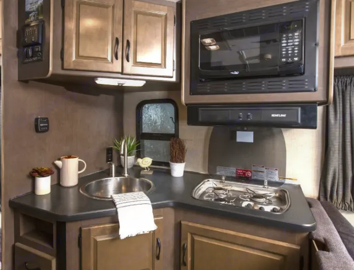 Explore this compact RV rental kitchen featuring a sink, microwave, two-burner stovetop, and ample cabinets.. Thor Majestic 2018