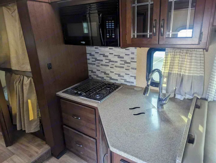 Cozy RV rental kitchen featuring a microwave, stove, sink, and bunk beds. Perfect for your next adventure!. Jayco Redhawk 2019