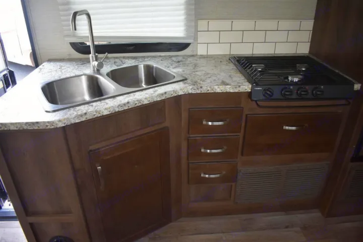 RV rental kitchen featuring a stainless steel double sink, granite-look countertop, gas stovetop, and dark wood cabinets.. Jayco Redhawk 2019
