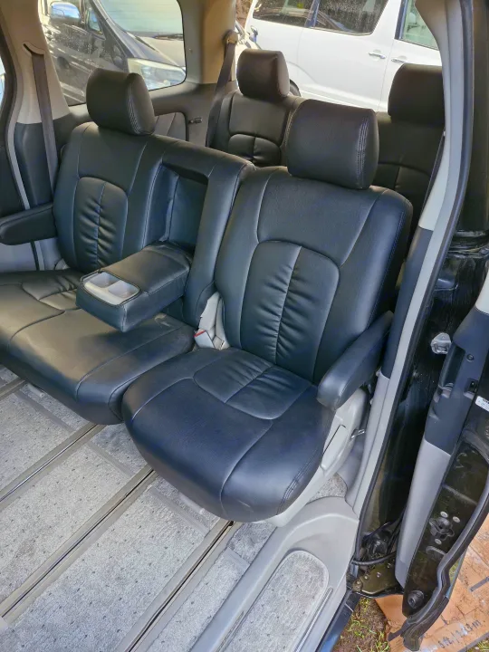 Comfortable black leather interior of an RV rental passenger van, featuring multiple rows of seating, armrests, and floor rails.. Toyota Alphard 2024