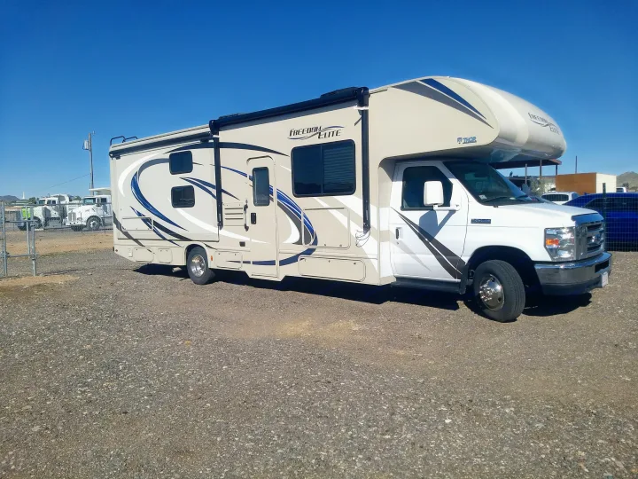 Explore the open road in this Thor Freedom Elite Class C RV rental, parked on a gravel lot under a clear blue sky.. Thor Motor Coach Freedom Elite 2019