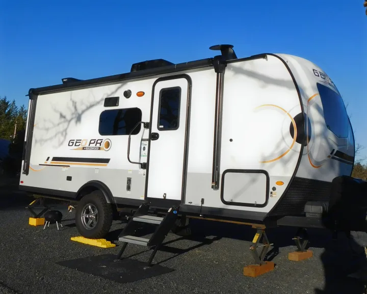 This white and gray GEO PRO travel trailer RV rental is set up at a sunny campsite with leveling jacks visible.. Forest River GeoPro 20BHS 2022