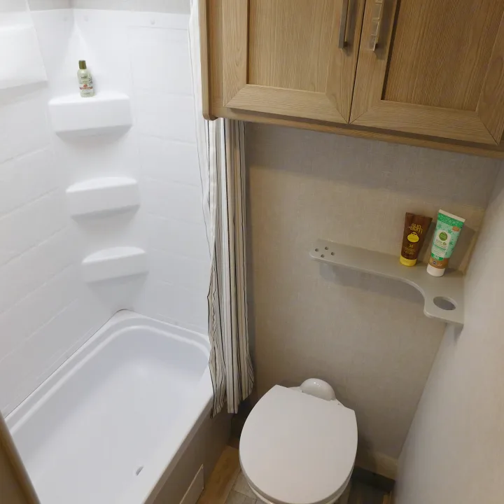 RV rental bathroom with a compact white shower/tub, toilet, and wooden overhead cabinets, offering essential amenities.. Forest River GeoPro 20BHS 2022