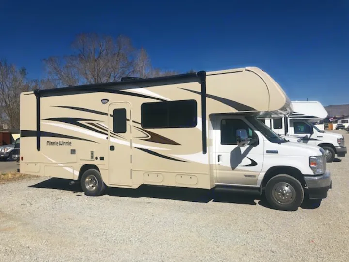 Side view of a Class C Winnebago Minnie Winnie RV, a great option for an RV rental. Parked on gravel on a bright day.. Winnebago Minnie Winnie 2024