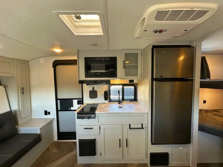 Spacious RV rental interior featuring a modern kitchen with stove, microwave, and fridge, plus comfy seating & bunk beds.. Forest River Salem FSX 2022