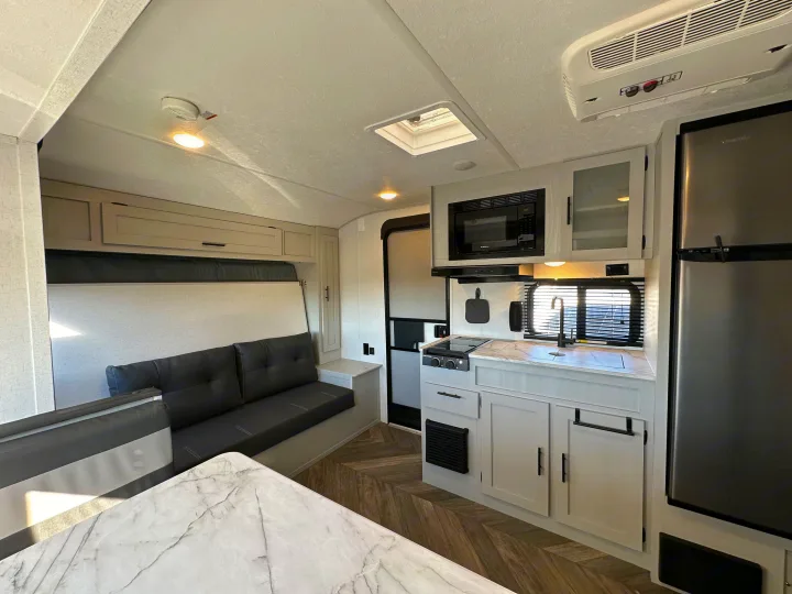 Modern RV rental interior: kitchen with sink, microwave, fridge; dining table & sofa converting to bed.. Forest River Salem FSX 2022