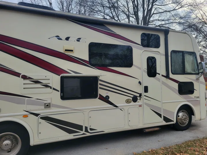 Side view of a beige ACE Thor rv rental, featuring bold red, black, and grey stripes, and multiple exterior compartments.. Thor A.C.E. 2018