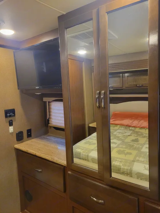 RV rental bedroom with TV, mirrored closet, storage, and bed. Practical, comfortable interior.. Thor A.C.E. 2018
