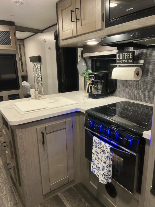 This RV rental's modern kitchen boasts a sleek sink, stove with blue lights, microwave, & coffee station, perfect for travel.. Heartland RVs Mallard 2022