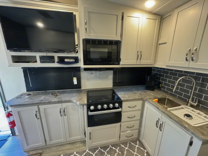 Step inside this modern RV rental featuring a full kitchen with light grey cabinets, black appliances, a sink, and a TV entertainment area.. Keystone Cougar Sport 2024