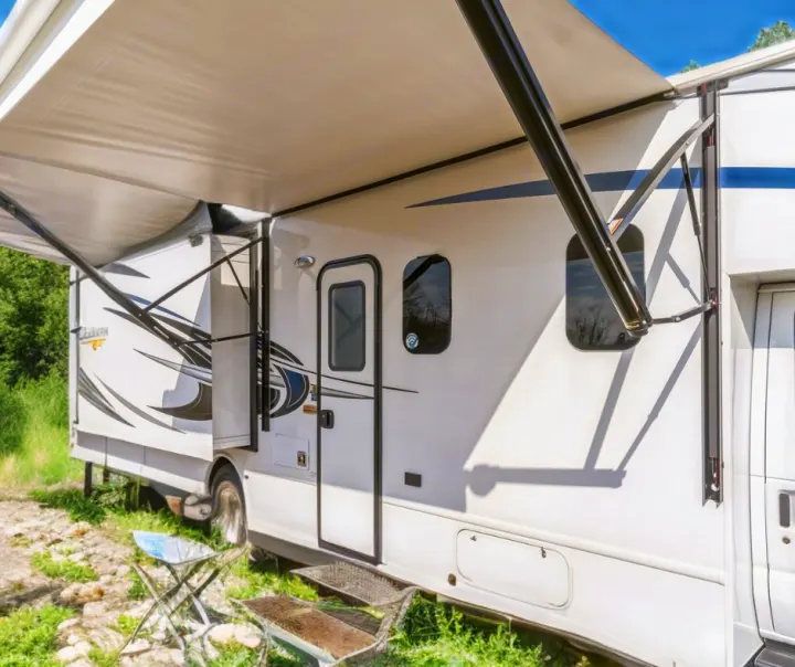 A white RV rental with its side awning and slide-out extended, set up for a comfortable outdoor adventure on grass.. Nexus RV Triumph 2022