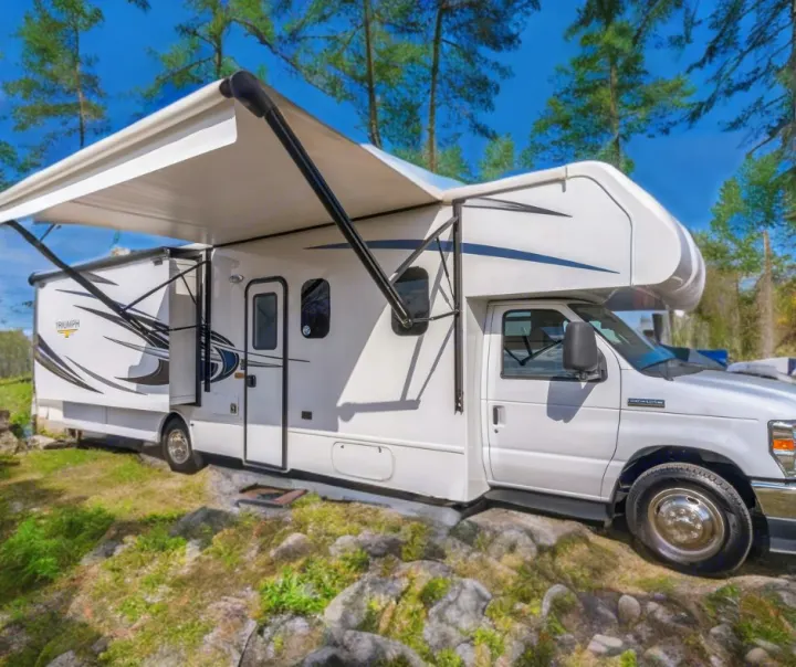 Experience outdoor adventures with this white RV rental, featuring an extended awning and slide-out at a scenic campsite.. Nexus RV Triumph 2022