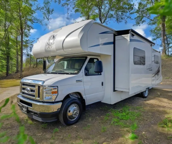 Experience outdoor travel with this white Nexus RV rental, a spacious motorhome parked in a lush, wooded area.. Nexus RV Triumph 2022