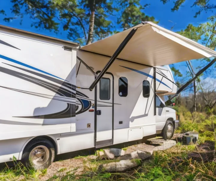 White Class C RV rental with extended awning parked at a sunny forest campsite, ideal for outdoor adventures.. Nexus RV Triumph 2022