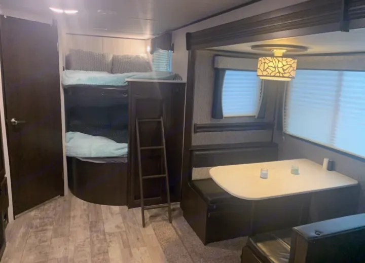 This RV rental interior features bunk beds with a ladder & a dinette with table and bench seating, ideal for family adventures.. Heartland Pioneer 2020