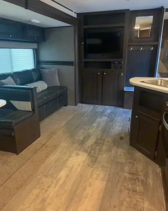 Modern RV rental interior: Living area with dark leather couch, TV, and kitchen space visible.. Heartland Pioneer 2020