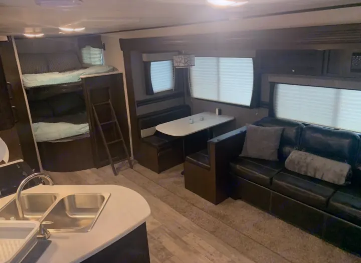 Spacious RV rental interior with bunk beds, a dinette, sofa, and kitchen sink, offering comfortable travel.. Heartland Pioneer 2020