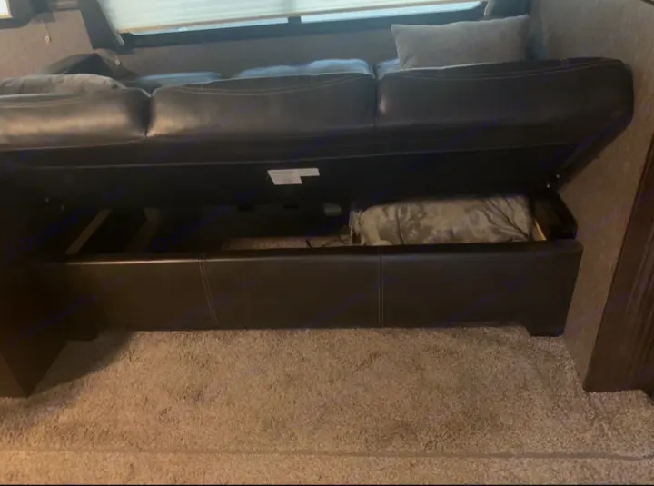 Black RV rental sofa bed partially open, showing pull-out mechanism and blanket storage underneath.. Heartland Pioneer 2020