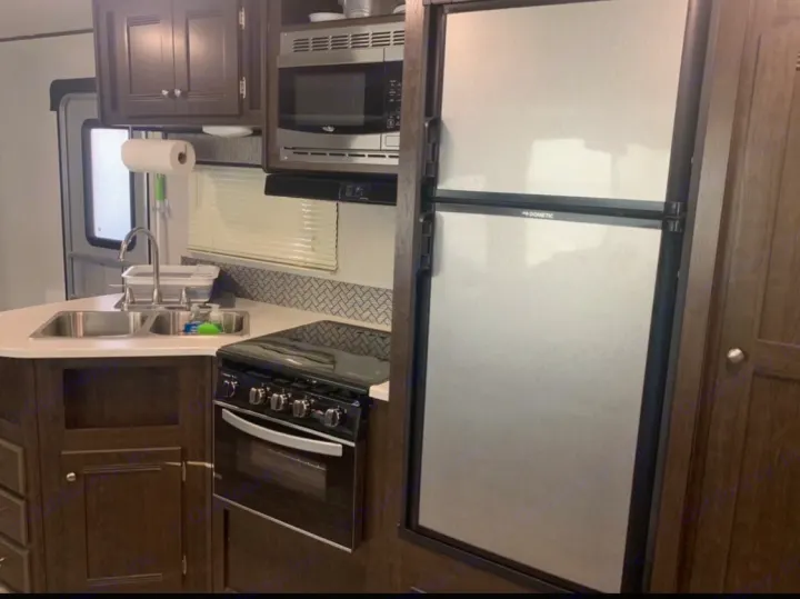 RV rental's compact kitchen with stainless steel appliances: Dometic fridge, microwave, stove, double sink, dark wood cabinets.. Heartland Pioneer 2020