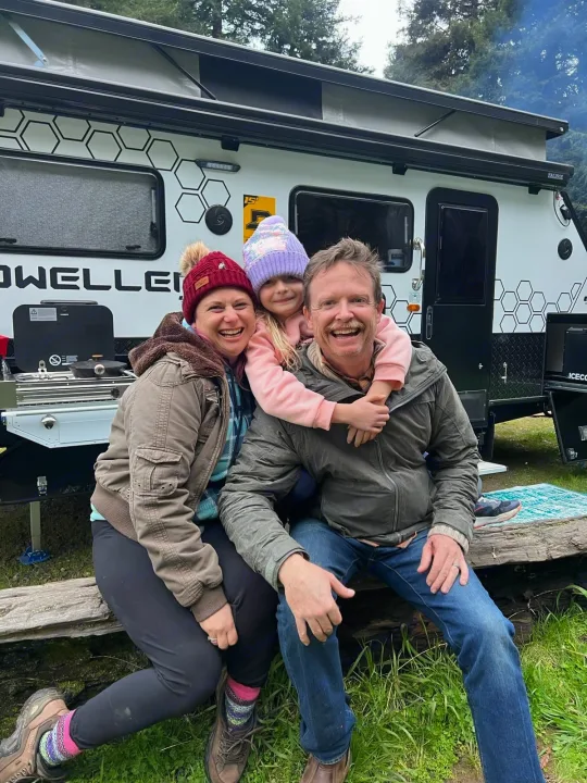 A happy family poses with their modern RV rental, a white travel trailer perfect for camping trips.. OBI OBI Popup Trailer 2022