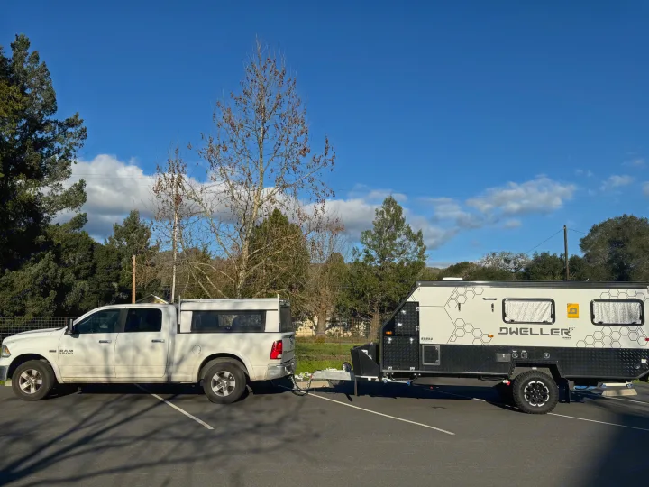 A white Ram pickup truck is towing a Dweller 15' travel trailer in a paved lot. A good look for an RV rental.. OBI OBI Popup Trailer 2022