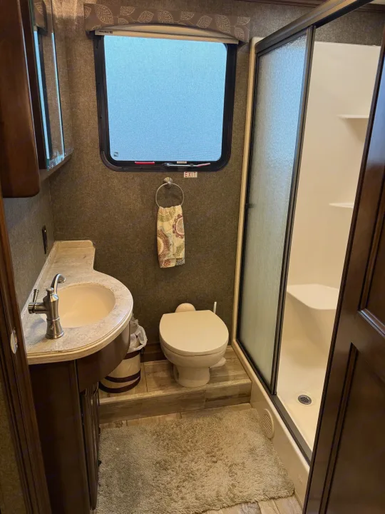 RV rental bathroom features: sink vanity, toilet, and glass shower. Emergency exit window is visible, ensuring safety and comfort.. Thor Venetian 2017