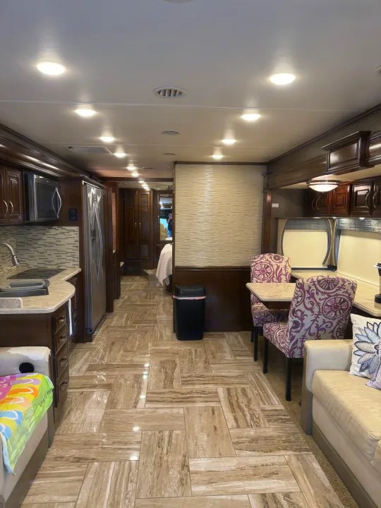 Warm wood tones and tiled floors in this RV rental's inviting kitchen, dining, and living area.. Thor Venetian 2017