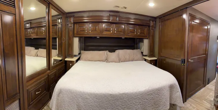 Luxurious RV rental bedroom with a large bed, elegant dark wood built-in storage, and mirrored closet doors.. Thor Venetian 2017