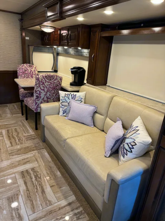Spacious RV rental interior: cream sofa, purple dining chairs, kitchen counter, & rich wood cabinets.. Thor Venetian 2017
