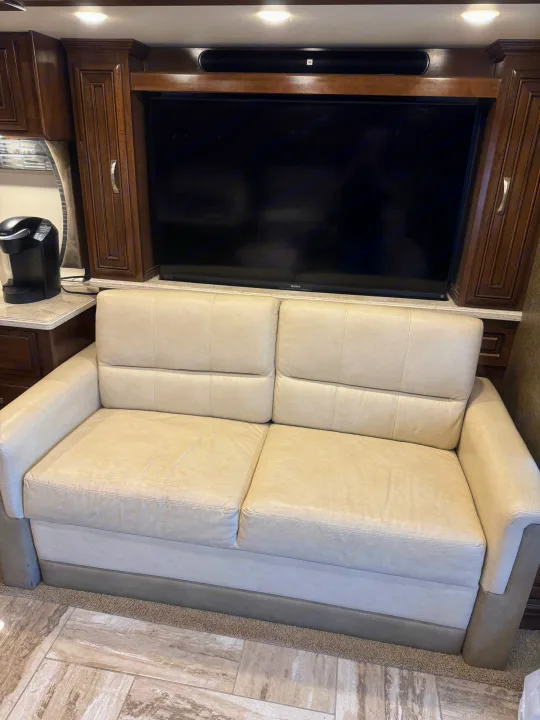 This RV rental interior features a comfortable light-colored sofa, flat-screen TV, Keurig, and rich wood cabinetry.. Thor Venetian 2017